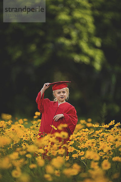 Lächelndes Mädchen im Graduiertenkleid steht inmitten gelber Blumen auf dem Feld