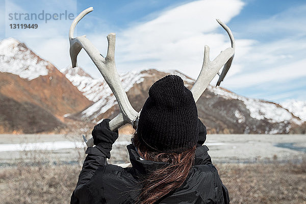Rückansicht einer Frau  die im Denali-Nationalpark ein Geweih gegen die Berge hält