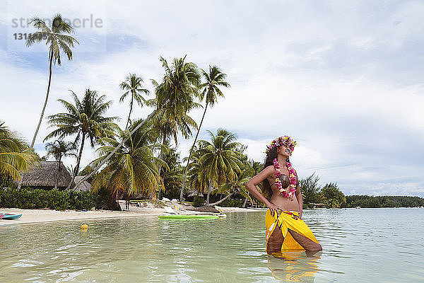 Lächelnde Frau in traditioneller Kleidung steht im Meer vor bewölktem Himmel