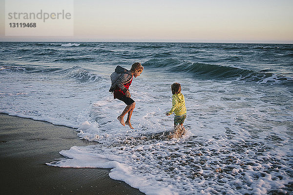 Geschwister spielen bei Sonnenuntergang am Strand am Ufer