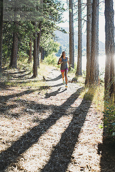 Frau rennt am sonnigen Tag an Bäumen vorbei auf dem Pfad