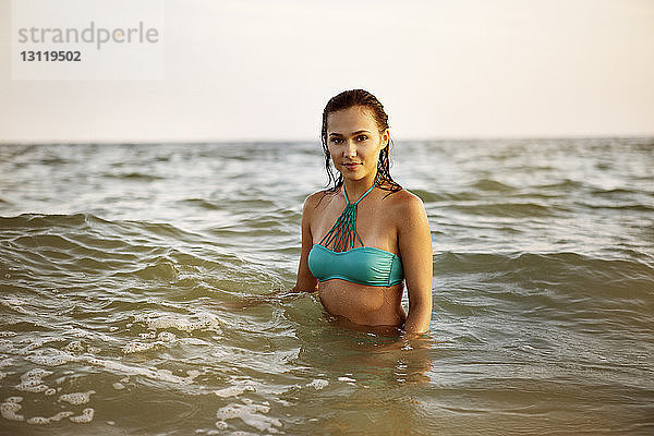 Porträt einer selbstbewussten Frau in blauem Bikini-Oberteil  die im Meer steht