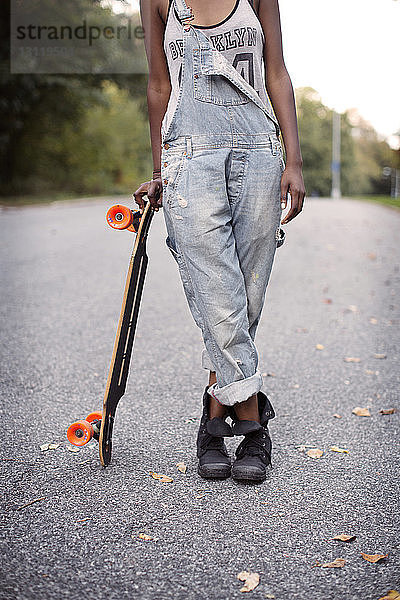Niedriger Teil einer Frau  die ein Skateboard hält und auf der Straße steht