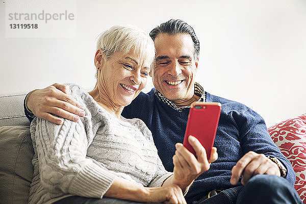Lächelndes älteres Paar  das zu Hause auf dem Sofa sitzend auf ein Smartphone schaut