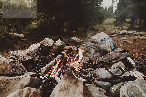 Textilien am brennenden Lagerfeuer inmitten von Felsen im Wald