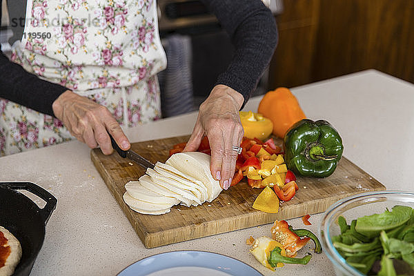 Mitschnitt einer Frau beim Käseschneiden während der Zubereitung von Speisen in der heimischen Küche