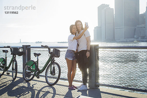 Glückliches Paar  das sich am sonnigen Tag beim Stehen am Fahrrad über das Mobiltelefon selbstständig macht