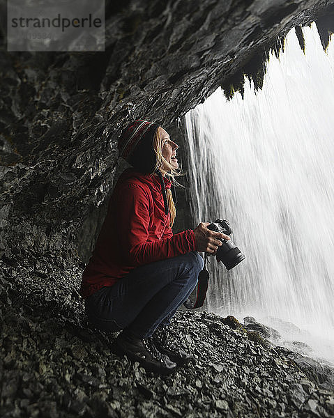 Fröhliche Wanderin schaut auf Wasserfall  während sie die Kamera hält