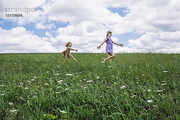 Seitenansicht von Schwestern  die auf einem Grasfeld vor bewölktem Himmel gehen