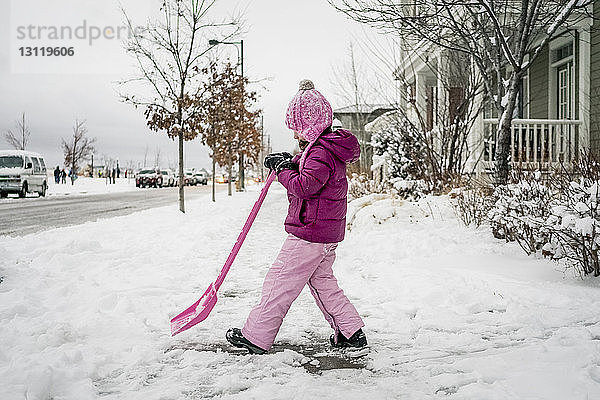 Seitenansicht eines Mädchens  das mit einer Schaufel Schnee von der Straße gegen den Himmel räumt