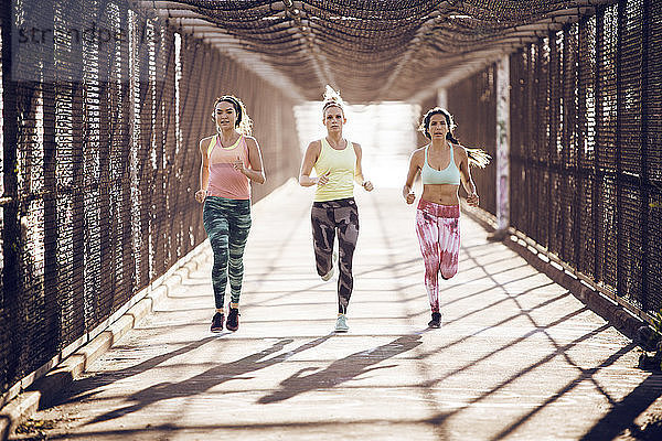 Athletinnen in voller Länge auf einer überdachten Brücke an einem sonnigen Tag joggen