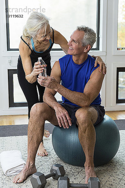Frau verschenkt Wasserflasche an Mann  der zu Hause auf Fitnessball sitzt