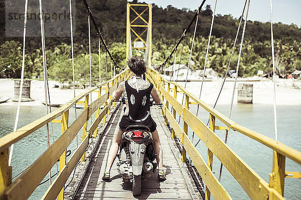 Rückansicht einer Roller fahrenden Frau auf der Brücke