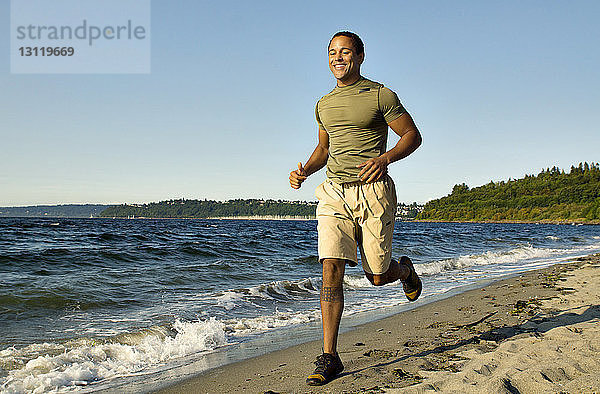 Fröhlicher Mann joggt am Ufer vor klarem Himmel