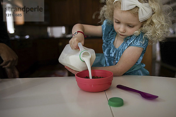 Mädchen gießt Milch in Schüssel auf den Tisch