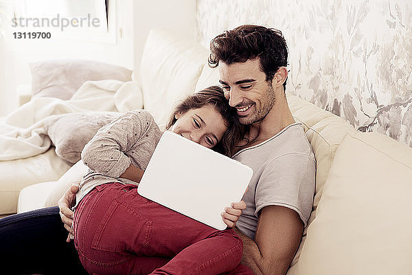 Glücklicher Vater und Tochter lesen digitales Tablett  während sie sich auf dem Sofa ausruhen