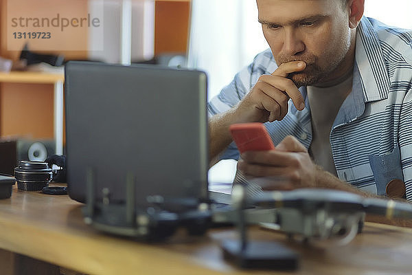 Ingenieur  der ein Mobiltelefon benutzt  während er im Büro am Tisch sitzt