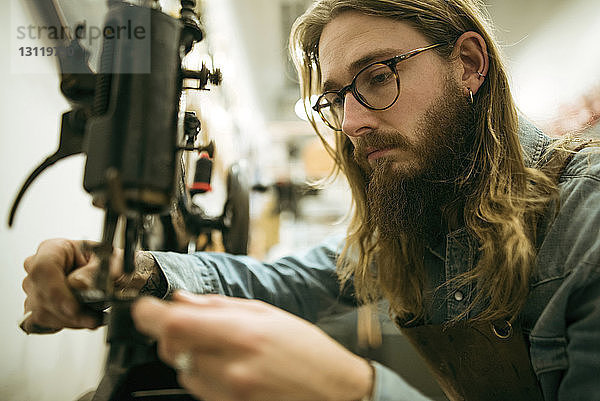 Seriöser Schuhmacher beim Einstellen der Nähmaschine in der Werkstatt