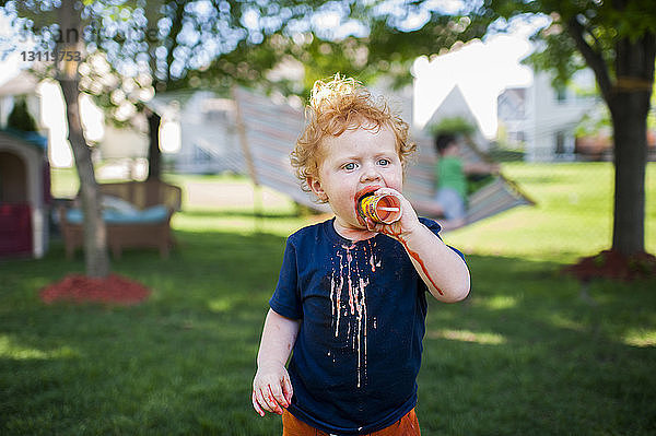 Süßer kleiner Junge isst Eiscreme  während er auf einem Grasfeld im Hof steht