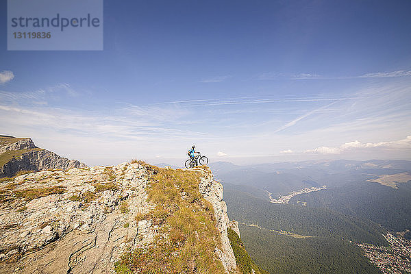 Fernansicht eines Mountainbikers mit Fahrrad  der auf einer Klippe gegen den Himmel steht