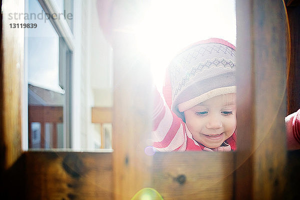 Babymädchen mit Kapuzenjacke durch Holzgeländer bei Sonnenschein gesehen