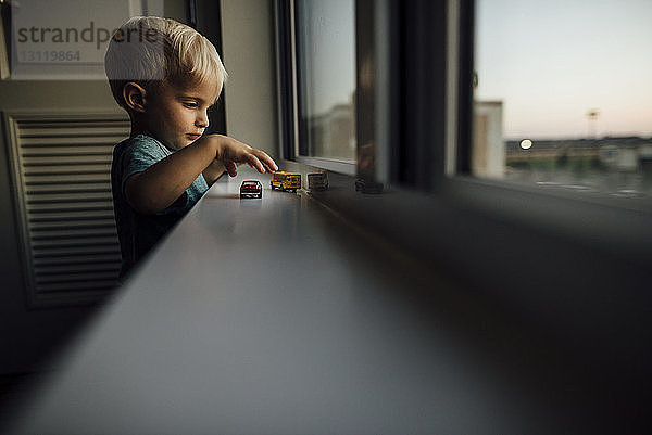 Seitenansicht eines kleinen Jungen  der zu Hause auf dem Fensterbrett mit Spielzeugautos spielt