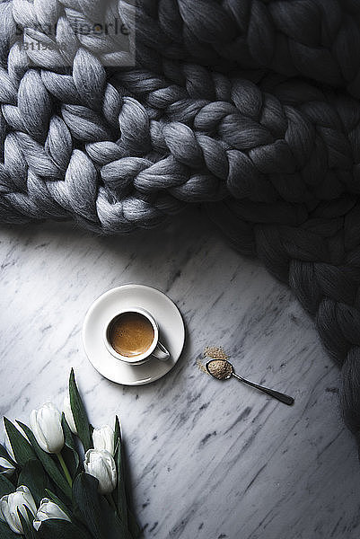 Draufsicht auf eine Kaffeetasse mit geflochtener Decke und Tulpen auf dem Tisch