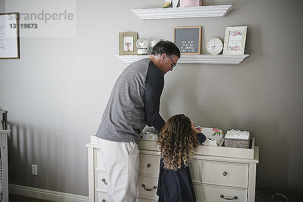 Vater und Tochter pflücken ein kleines Mädchen  das zu Hause auf einem Schrank liegt