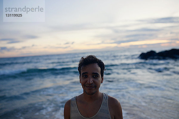 Porträt eines Mannes  der bei Sonnenuntergang am Meer steht