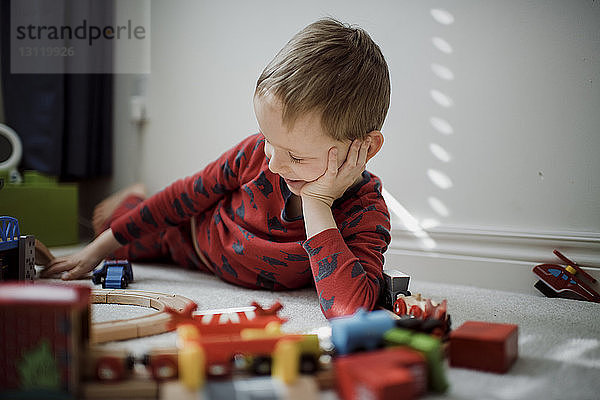 Junge mit dem Kopf in der Hand spielt mit einer Modelleisenbahn  während er zu Hause auf dem Teppich liegt