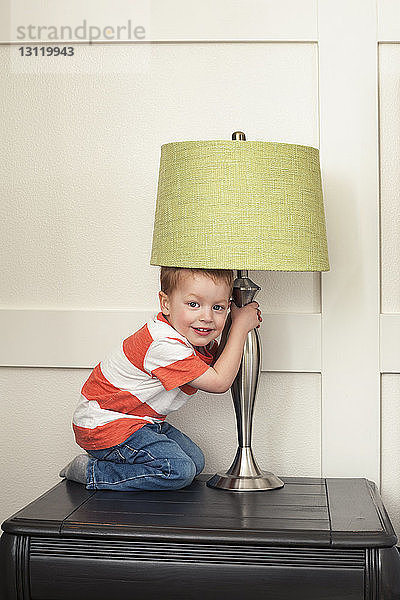 Porträt eines Jungen  der mit Lampenschirm auf dem Tisch hält und spielt