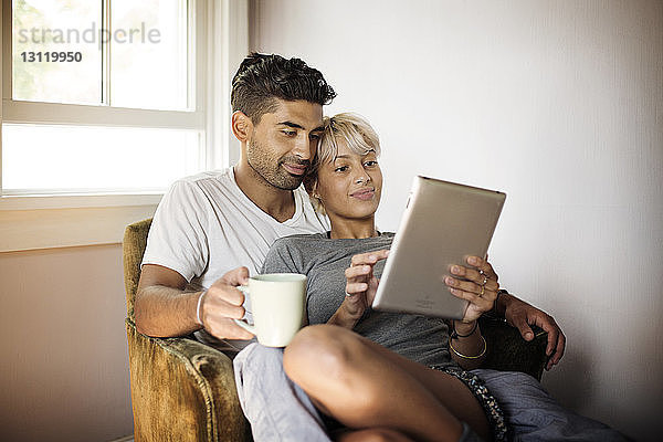 Junges Paar benutzt Tablet-Computer  während es zu Hause auf einem Sessel sitzt