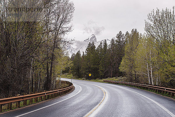 Leere Landstraße zwischen Bäumen gegen den Himmel im Grand-Teton-Nationalpark