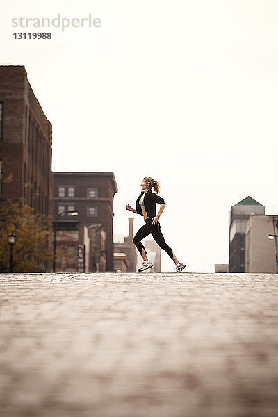 Seitenansicht einer Frau  die auf der Straße der Stadt bei klarem Himmel joggt