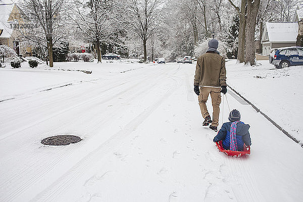 Rückansicht eines Schlitten fahrenden Vaters auf schneebedeckter Strasse