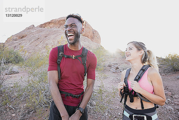 Glückliche Freunde mit Rucksäcken  die lachen  während sie vor Felsformationen stehen