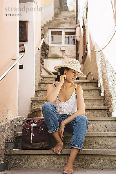 Nachdenklicher Tourist mit Hut  während er mit dem Rucksack auf Stufen in der Stadt sitzt