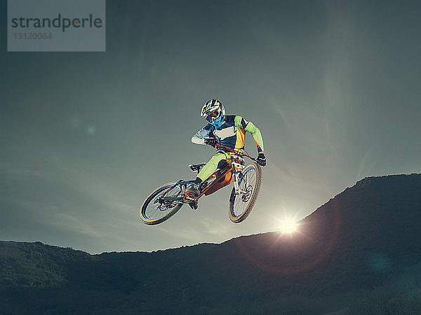 Niedrigwinkelansicht eines Bikers  der bei Sonnenuntergang einen Stunt gegen den Himmel macht