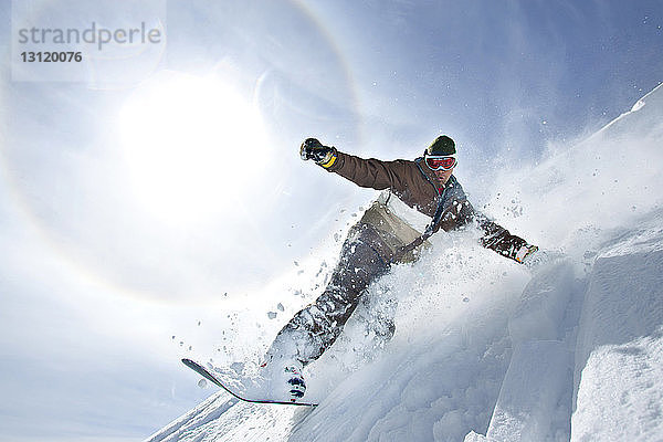 Mann beim Snowboarden auf dem Berg gegen den Himmel an einem sonnigen Tag
