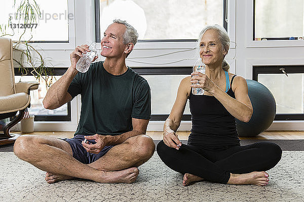 Lächelndes Paar trinkt beim Sport zu Hause Wasser aus Flaschen