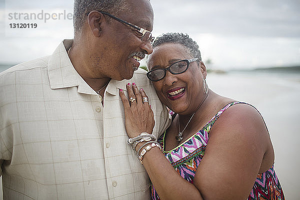 Glückliches älteres Ehepaar steht am Strand vor bewölktem Himmel