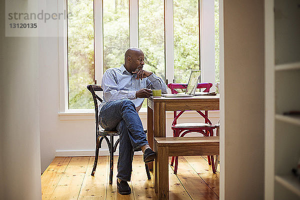 Älterer Mann benutzt Laptop beim Kaffeetrinken zu Hause