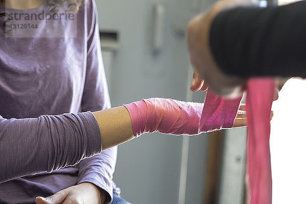 Ausschnitt einer Trainerin  die im Fitnessstudio die Hand einer Athletin mit Armband umwickelt