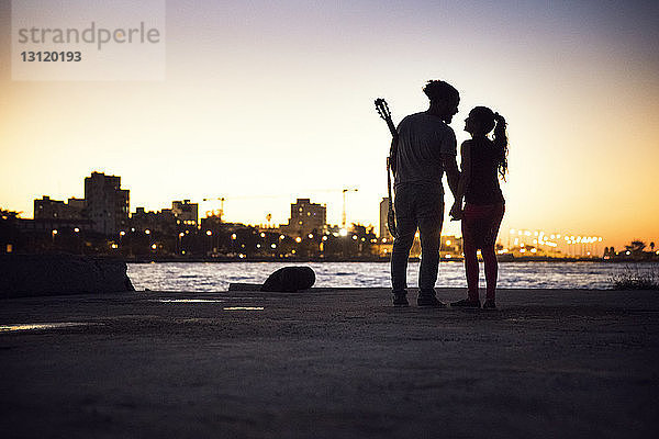 Silhouettenpaar steht am Seeufer vor klarem Himmel bei Sonnenuntergang