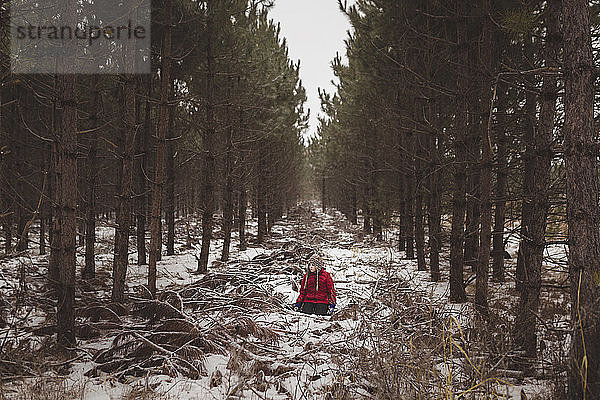 Sorgloses Mädchen sitzt im Winter inmitten von Bäumen im Wald