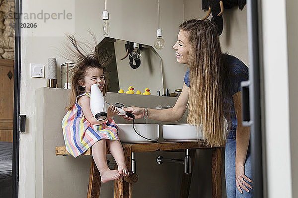 Niedriger Blickwinkel auf die Mutter  die das Haar ihrer glücklichen Tochter trocknet  die zu Hause auf dem Waschbecken im Badezimmer sitzt