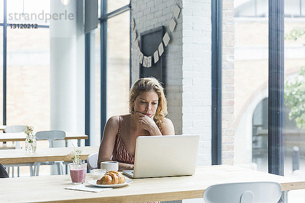 Frau mit Hand am Kinn mit Laptop-Computer  während sie im Café sitzt
