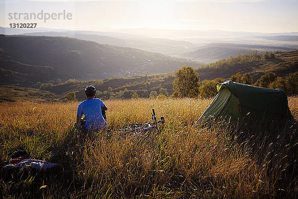 Rückansicht eines Mannes  der im Zelt auf einem Grasfeld gegen den Himmel sitzt