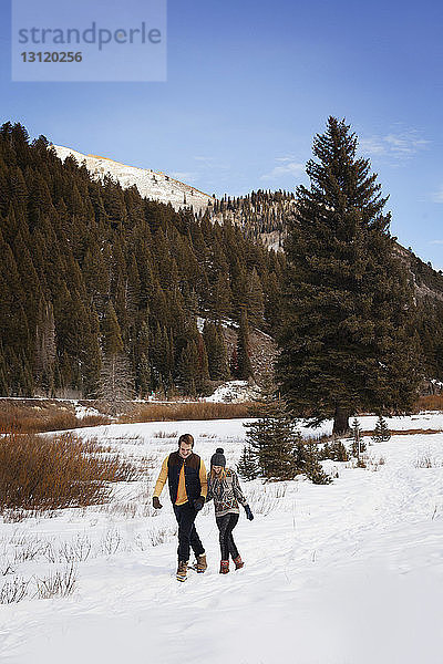 Junges Paar geht auf schneebedecktem Land gegen den Himmel