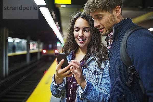 Ehepaar benutzt Mobiltelefon  während es in der U-Bahn-Station steht